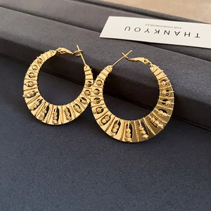 Macro shot of large gold-plated twist hoop earrings with intricate fan-shaped details