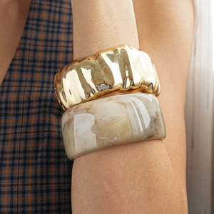 Detail of chunky gold irregular metal bangle and grey marble resin cuff on model wrist