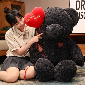 Macro detail of large black curly plush teddy bear holding a red heart balloon with embroidery