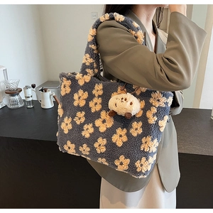 Detail of navy plush tote bag with yellow flowers and a cute animal charm in a cafe