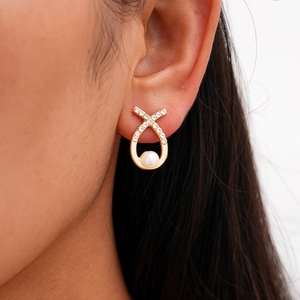 Close-up of golden ribbon stud earring with sparkling crystals and a white round pearl