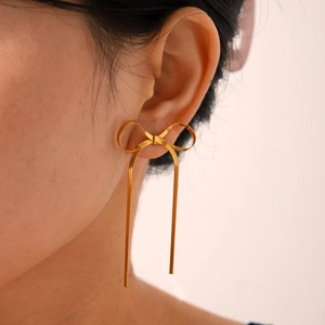 Close-up of golden bow long tassel earrings on a model showing smooth metal snake chain detail