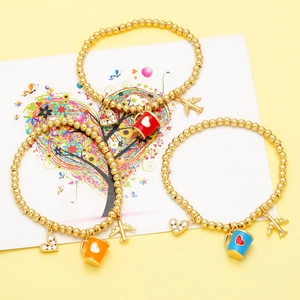 Detail view of gold beaded bracelets with airplane, crystal heart, and cup charms