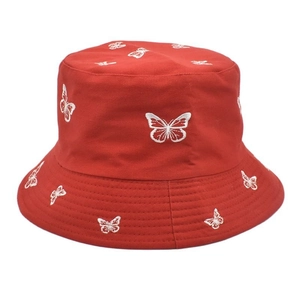 Vue détaillée de broderies papillon blanches sur le tissu rouge d'un chapeau bob en coton
