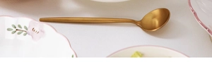 Detail view of a sleek golden metal spoon resting on a textured white dining table