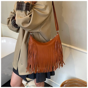 Caramel leather crossbody bag with tassel fringe detail worn by a model in casual attire