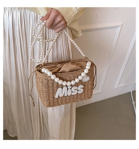 Detail of woven straw bucket bag with pearl handle and rhinestone MISS letters