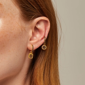 Detail of gold huggie earrings with black zircon square and round charms on ear
