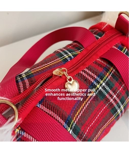 Detail of a red plaid bag featuring a heart-shaped gold zipper pull and woven strap