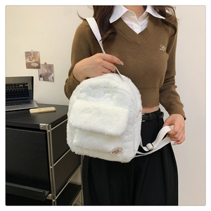 Primer plano de pequeña mochila de felpa blanca con etiqueta 'good luck' en fondo suave