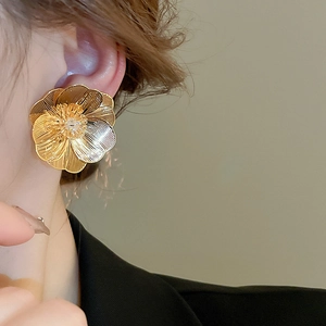 Close-up of golden floral earrings with zircon center and brushed metal texture on a model