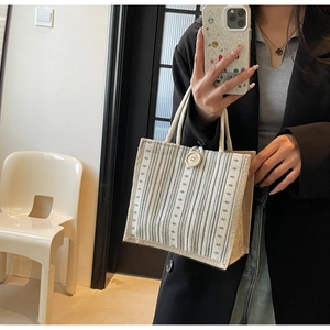 Detail of beige striped linen tote bag with decorative button and thick rope handles