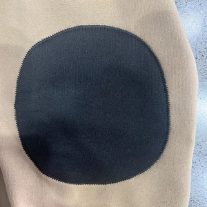 Close-up of khaki knit fabric featuring a black circular decorative patch on the sleeve