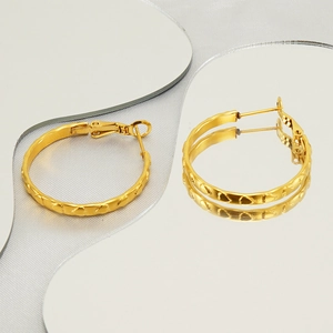 Detail of 18k gold heart embossed hoop earrings on modern mirrored decorative surfaces