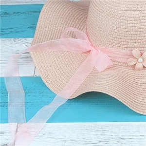 Detail of pink straw hat featuring organza ribbon bow and small pearl flower ornament