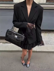 Detail of elegant black lace gloves paired with a sleek faux leather handbag and blazer
