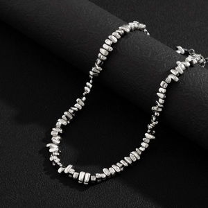 Men's silver irregular beaded necklace displayed on a textured pedestal with a dark background