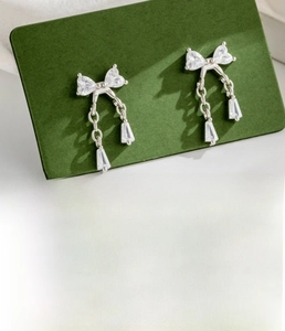 Detail of silver bow pendant earring with zircons on dark green display card