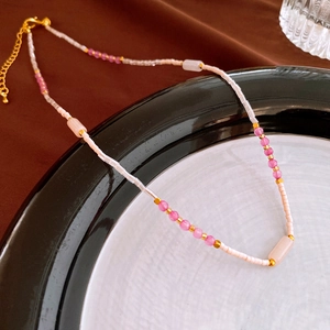 Detail of beaded necklace with pink stones and golden clasp on a ceramic plate