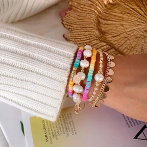 Detail of layered bohemian bracelets with pearls, rainbow clay beads and charms on model