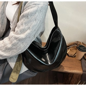 Close-up of black glossy PU leather shoulder bag on a model in a minimalist setting