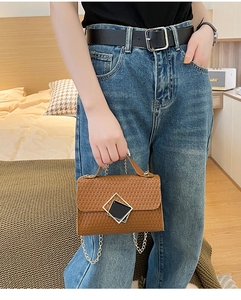 Detalle de bolso marrón grabado con hebillas plateadas y correa de cadena dorada