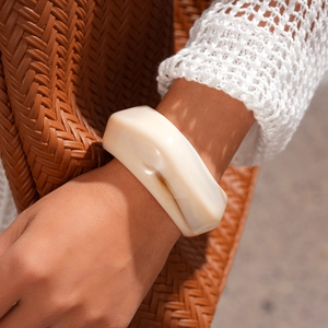 Detail shot of wide geometric cream acrylic cuff bracelet on model with floral sleeve
