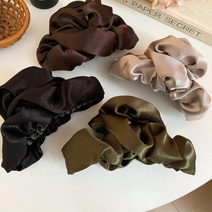 Detailed view of large pleated satin hair claws in black, brown, green, and gold colors