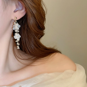 Close-up of floral tassel earrings with white petals and rhinestones on a model