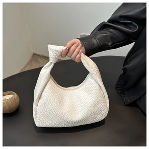 Close-up of white woven pattern faux leather tote bag held against dark leather jacket