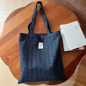 Détail du sac cabas en denim bleu foncé avec texture chevron et étiquette vintage sur bois