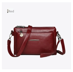 Close-up of deep red textured faux leather crossbody bag with three zipper compartments