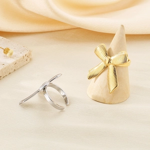 Detailed view of gold and silver bow rings with silk ribbon texture on wood stand