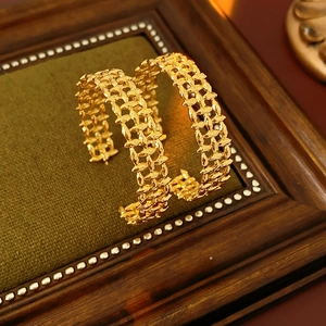 Close-up of golden hollow C-shaped earrings with double-loop design on vintage wood