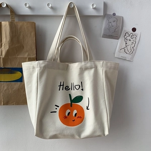 Detail of cream canvas tote bag featuring orange cartoon print and Hello text