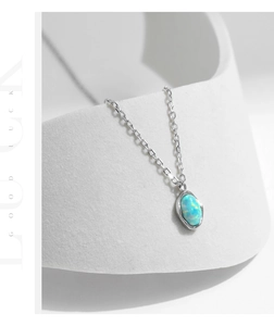 Macro detail of silver necklace with iridescent blue oval opal pendant on white stand