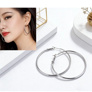 Close-up of polished silver oversized hoop earrings worn by a model and on a stand