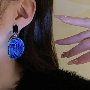 Nahaufnahme von blauen Vintage-Ohrringen mit Textur, getragen von einem Model im Licht