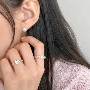 Detail of silver heart rings and pearl earrings worn with pink knit sweater