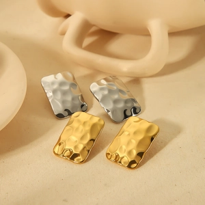 Close-up of gold and silver rectangular earrings with irregular hammered metal texture