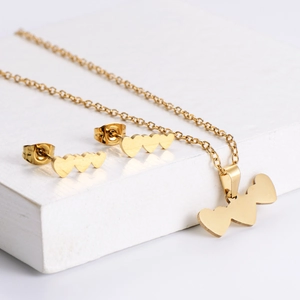 Polished gold heart jewelry set including necklace and stud earrings on white blocks