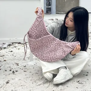 Outdoor model holding pink leopard print suede shoulder bag with adjustable strap details