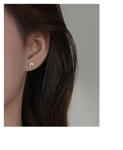 Close-up of a silver cat paw stud earring with white zircons on a model's ear