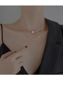 Detail view of double-layer gold necklace featuring a baroque pearl on a woman's neck