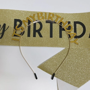 Close-up of golden glitter IT'S MY BIRTHDAY headband and ceremonial party sash