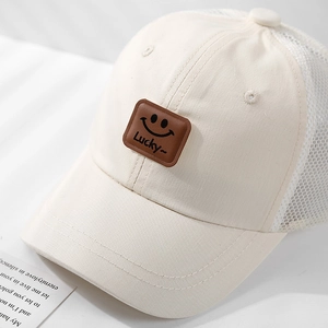 Detail of breathable mesh stitching and leather smiley patch on beige kids baseball cap