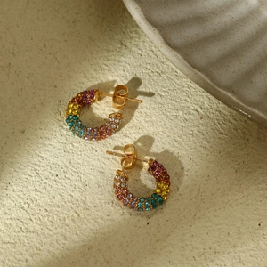 Rainbow rhinestone C-shaped hoop earrings with gold finish on a textured background