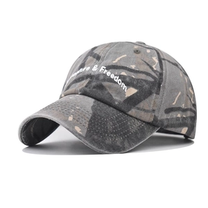 Close-up of white Adventure & Freedom embroidery on washed camouflage baseball cap fabric