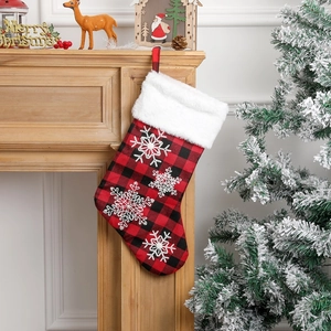 Red and black plaid Christmas stocking with white snowflake embroidery hanging on fireplace