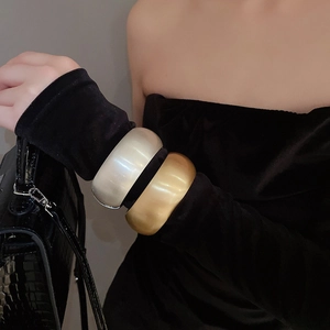 Detail of matte gold and silver wide open bangles shown on a model with black velvet dress